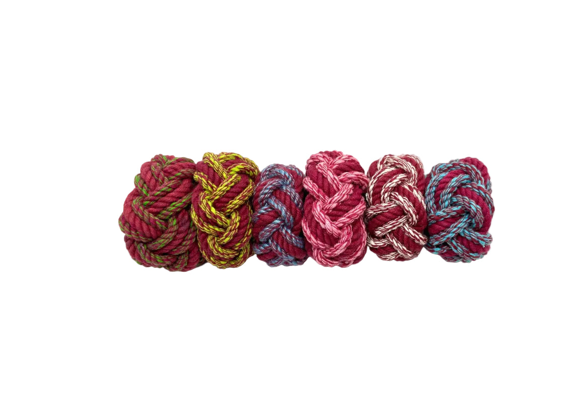 Four knotted yarn balls in red, yellow, pink, and blue on a white background