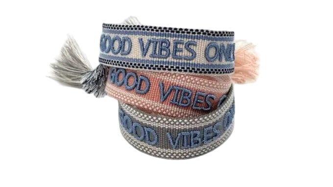 A collection of woven cotton friendship bracelets with the text 'GOOD VIBES ONLY' embroidered on them, displayed in a spiral stack with different bracelets showing the text in blue and black colors.