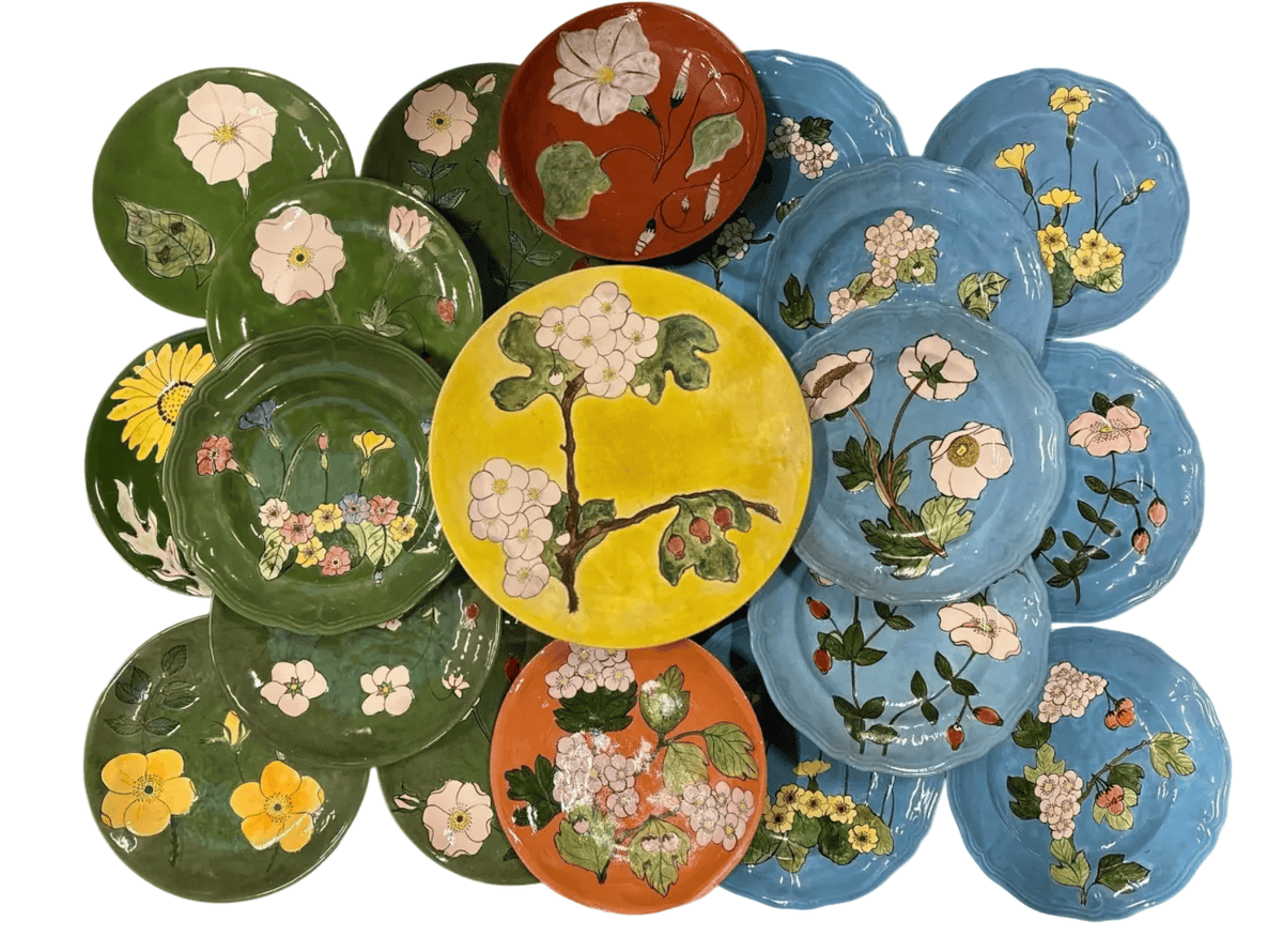 A collection of hand-painted ceramic plates arranged in a cluster, each featuring different floral and botanical designs in vibrant colors including green, blue, yellow, orange, and red.