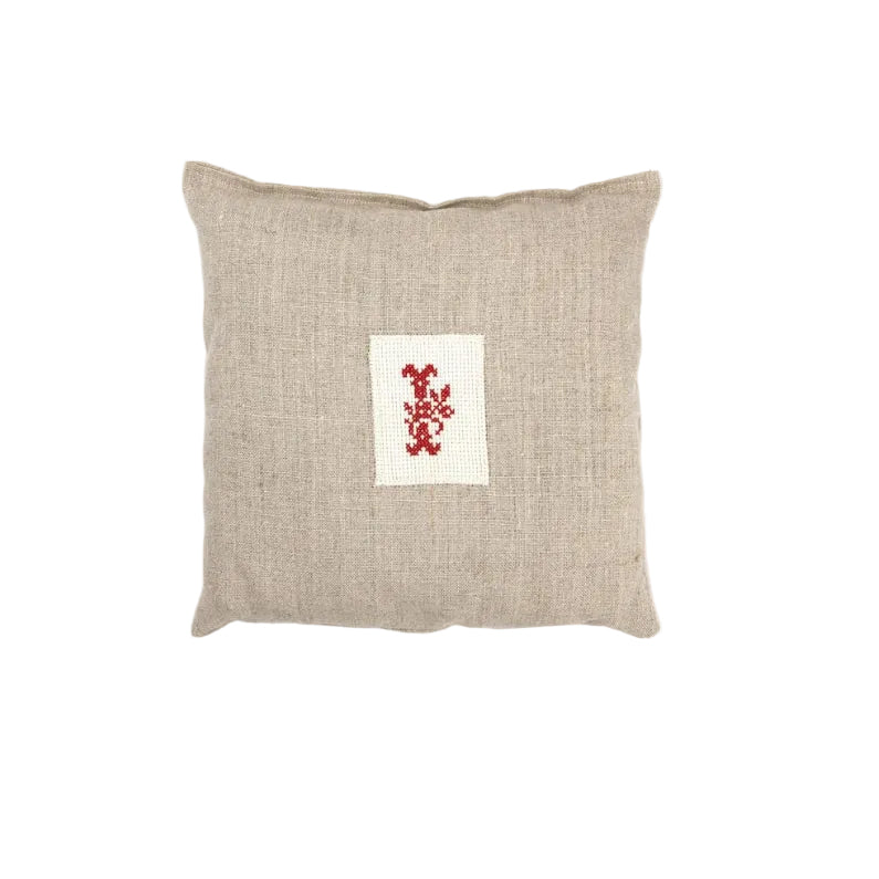 Beige pillow with a red and white embroidered design on a white background