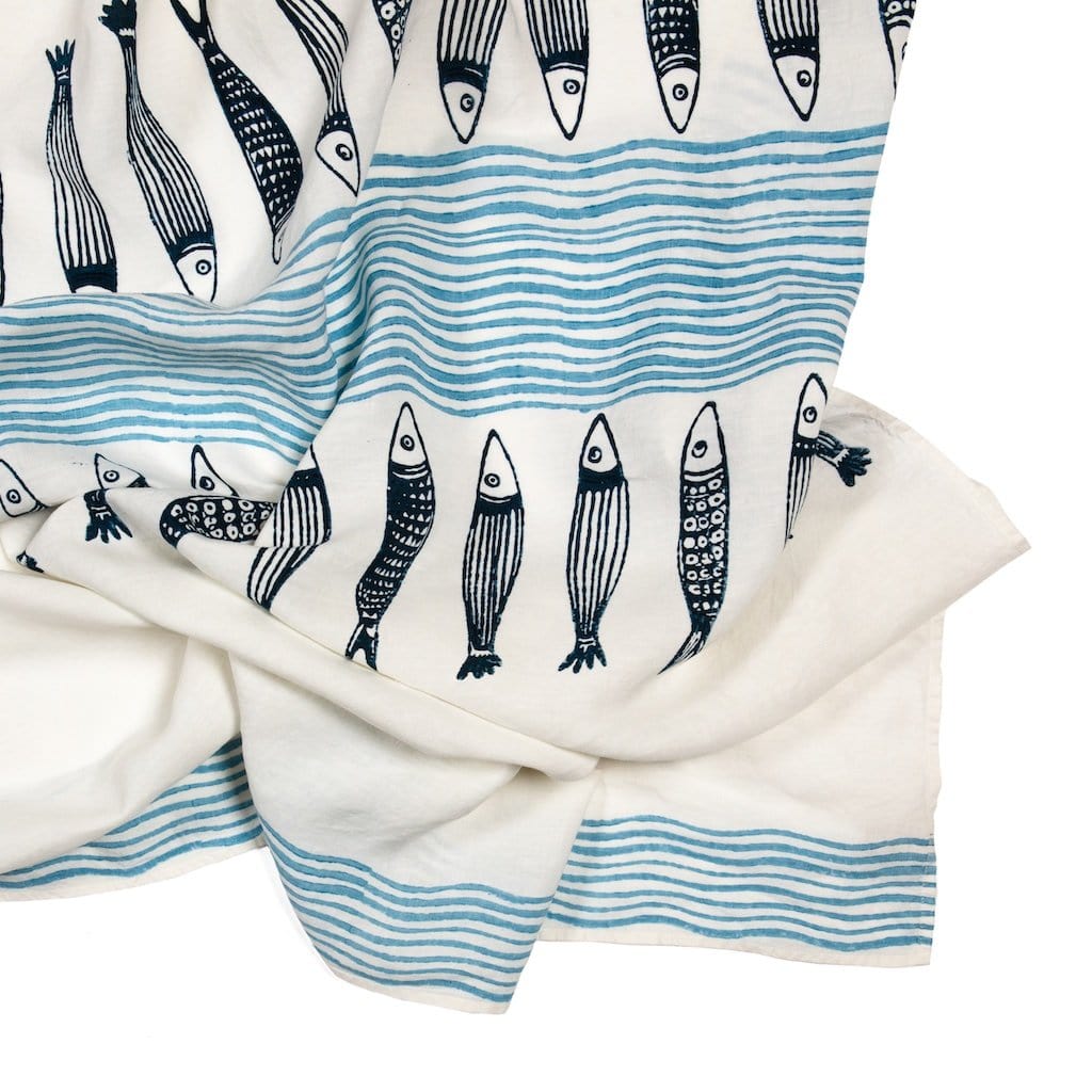 A traditional linen tablecloth featuring a pattern of hand-stamped fish motifs, predominantly in blue and white colors, with a striped border.