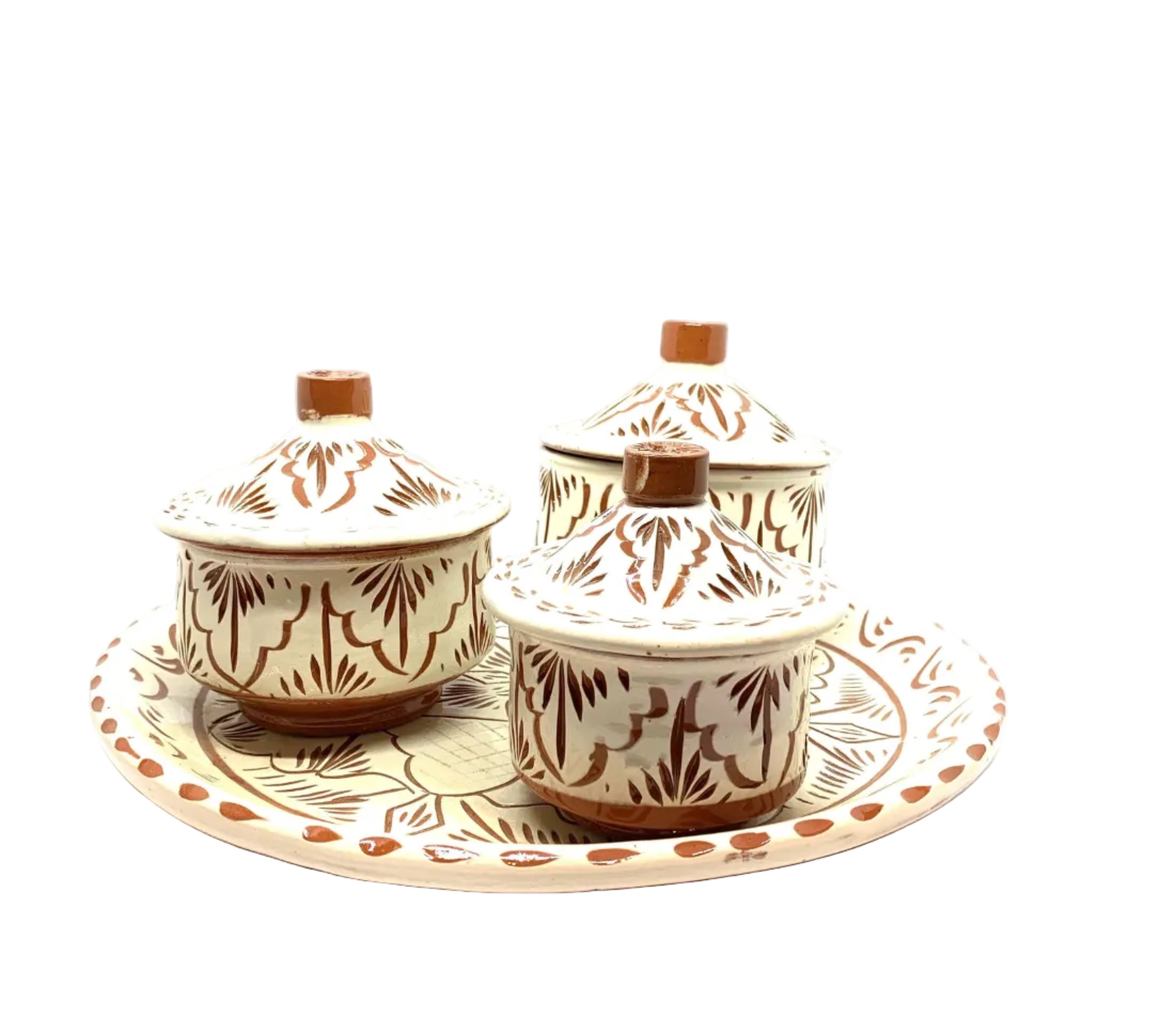 A set of three ceramic pots in different sizes, with hand-engraved floral and geometric patterns, placed on a matching green and beige patterned tray.