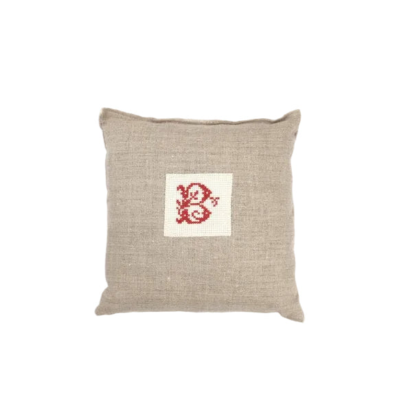 Beige pillow with a red and white intital on a white background